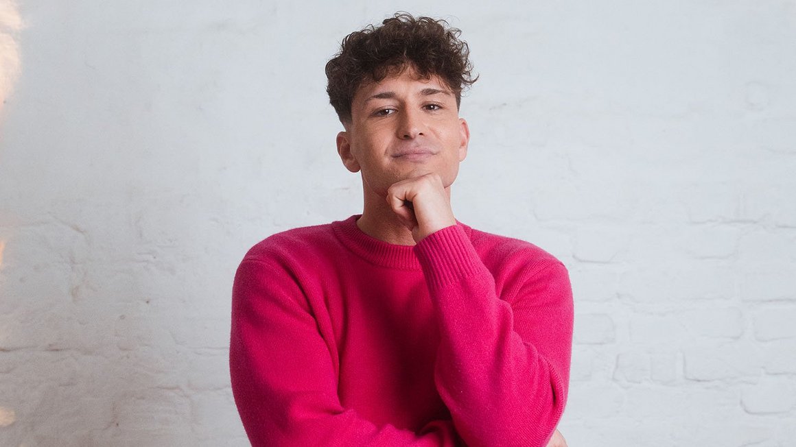 Uomo col maglione rosa guarda pensieroso la fotocamera