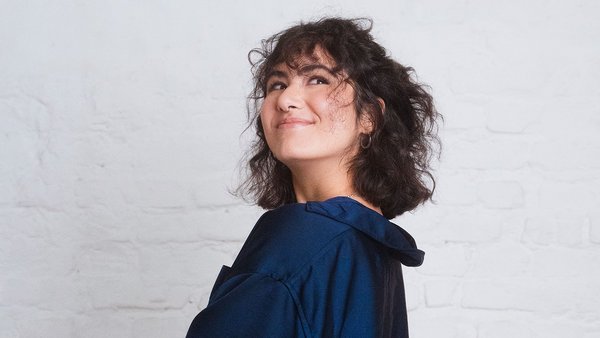 La regola 50 30 20 funziona anche se non si guadagna molto? Donna dallo sguardo birichino con camicia blu e capelli castani guarda in alto.