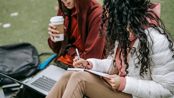 Due studentesse studiano insieme sedute su un prato 