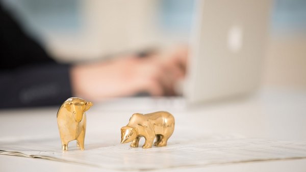 Statuette dorate di un toro e un orso davanti a un laptop su una scrivania