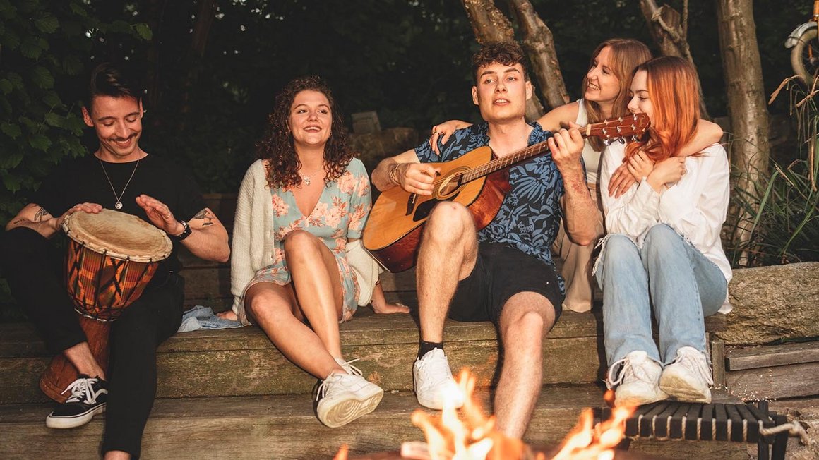 Quattro amici siedono insieme intorno a un falò e suonano la chitarra