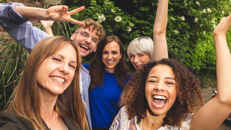 Cinque amici in piedi vicini tra loro che ridono davanti all’obbiettivo