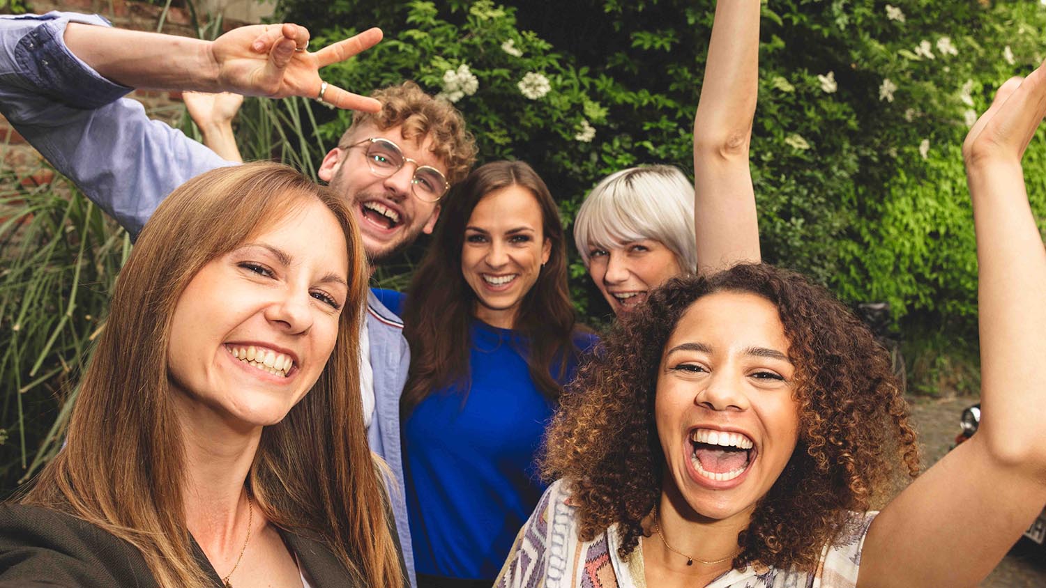 Cinque amici in piedi vicini tra loro che ridono davanti all’obbiettivo