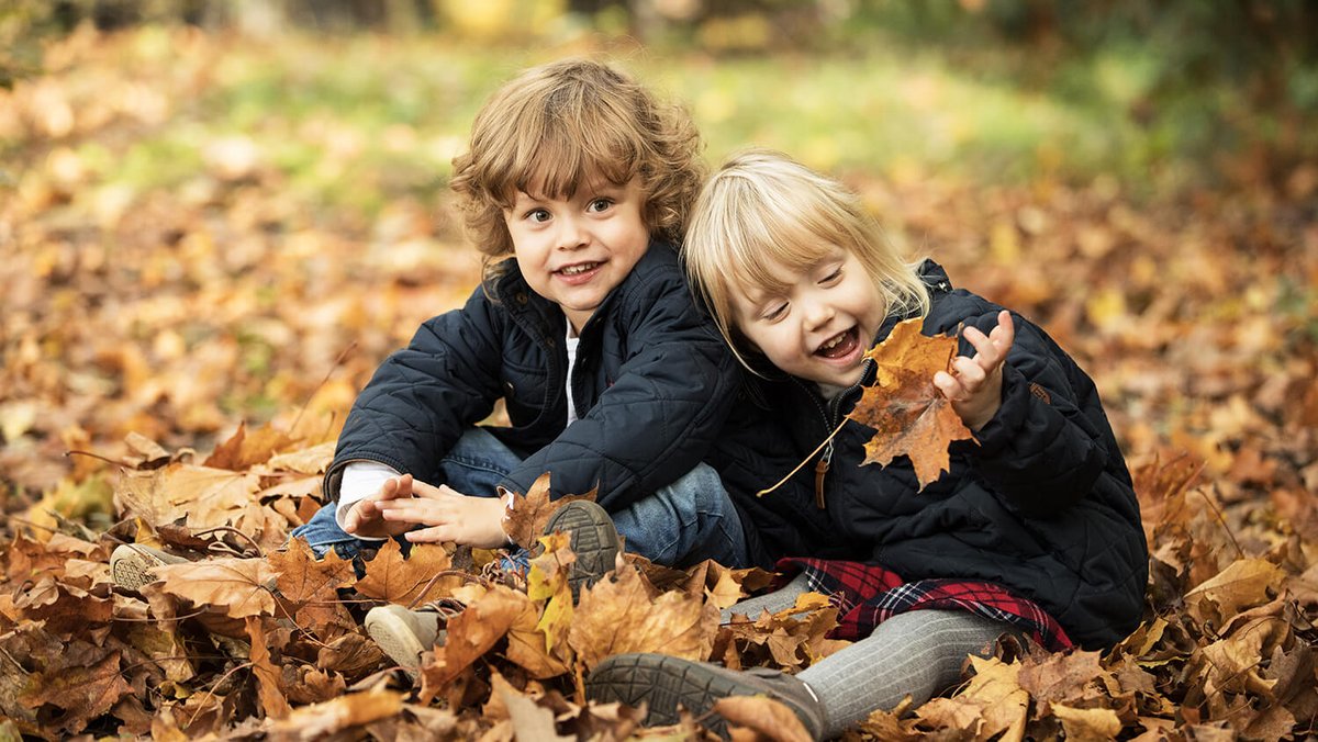 Due bambini seduti tra foglie autunnali