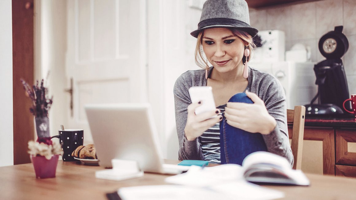 Giovane donna al tavolo con smartphone, taccuino e documenti per compilare il quaderno dei conti di casa